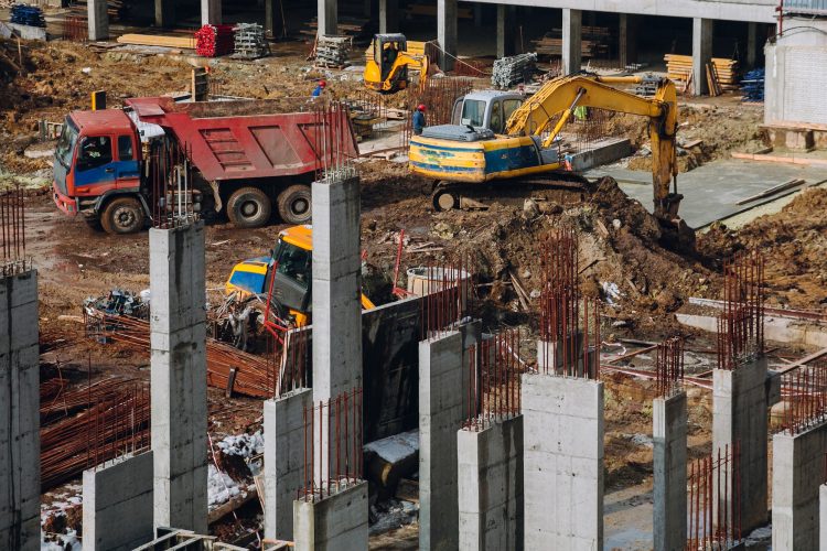 Crane beam machinery and bulldozer on building construction site on background of dirty ground