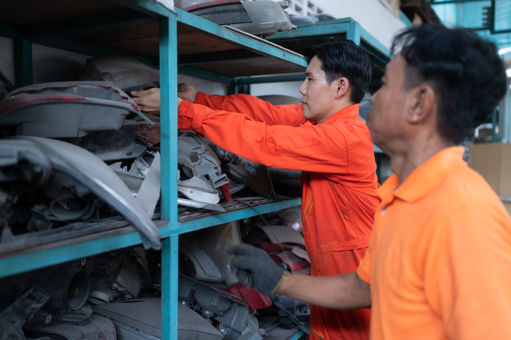 Two mechanics are selecting automobile parts, car headlights, from a spare parts warehouse